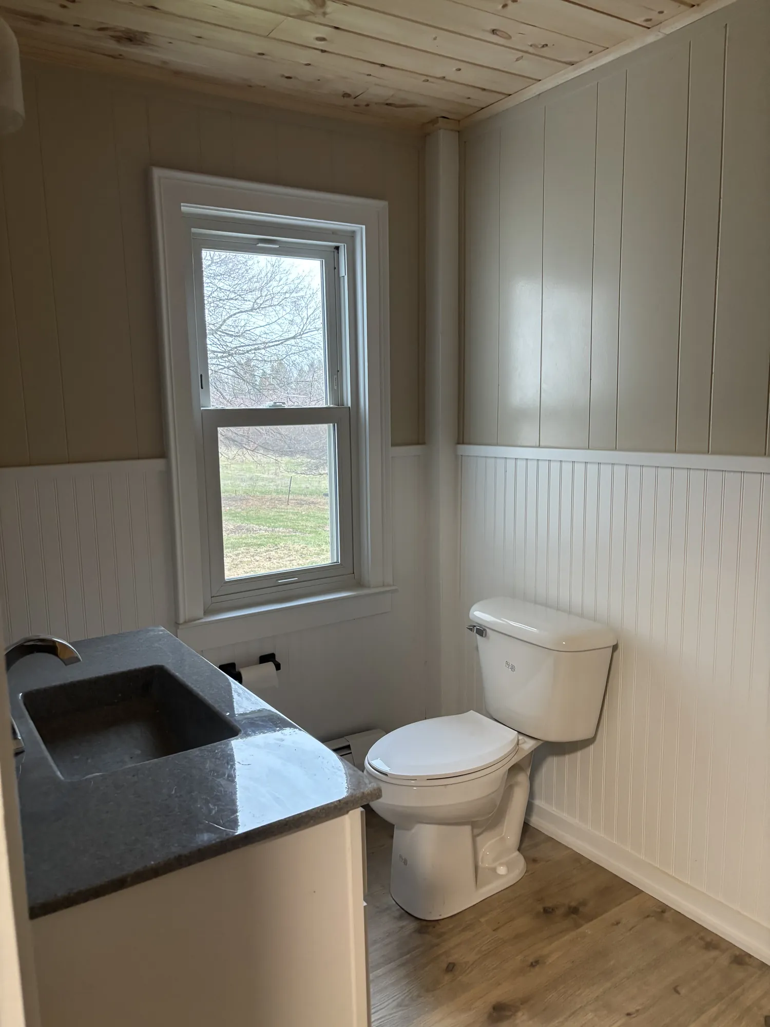 Bathroom with a white vanity and dark gray top, a white toilet, beadboard wainscot, painted paneling and a pine ceiling