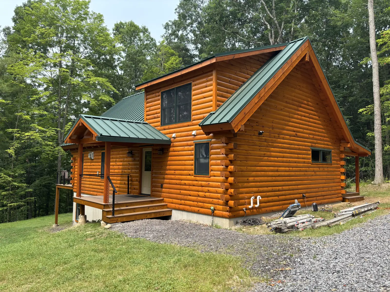 Log cabin with warm amber finished logs, green metal roof and covered entry porch on a grassy wooded lot